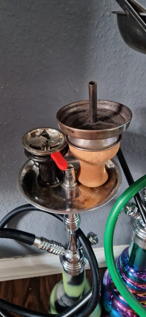 Shisha mit Glasbowl, Kohle und Schlauch auf einem Tisch.