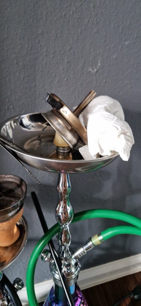 Shisha mit Glasbowl, Schlauch und Zubehörtasche auf Tisch.