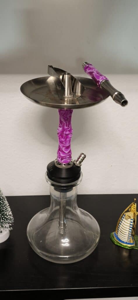 Shisha mit Glasbowl, Metallaufsatz und Dampfzubehör auf Tisch.