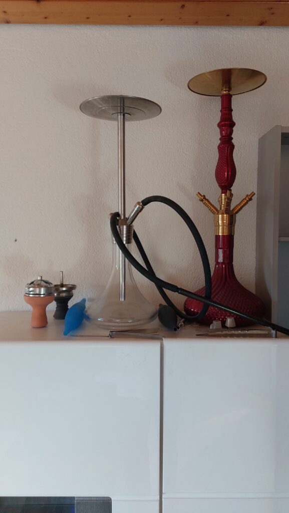 Shisha mit rotem Shishabowl, Metallrohr und Zubehör auf Tisch.