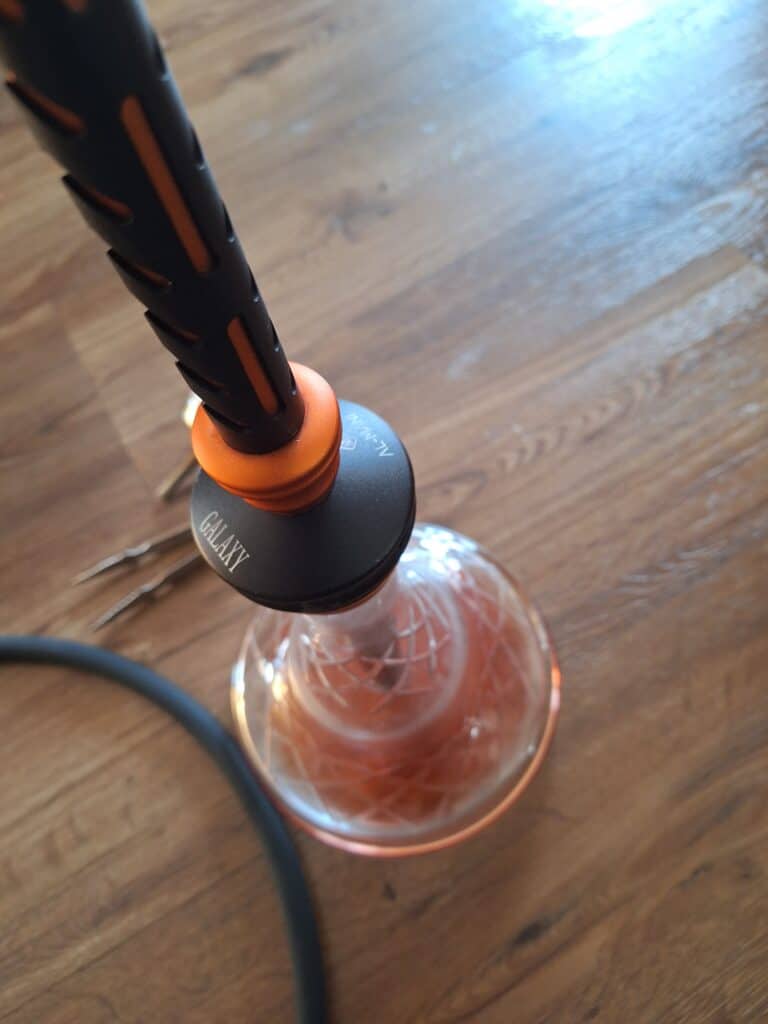 Shisha-Glasbowl mit Rauchsäule auf Holztisch.