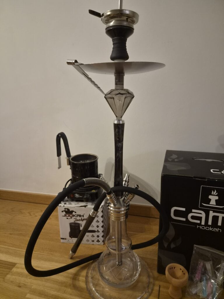 Shisha mit Glasbowl, Schlauch und Zubehör auf Holztisch.