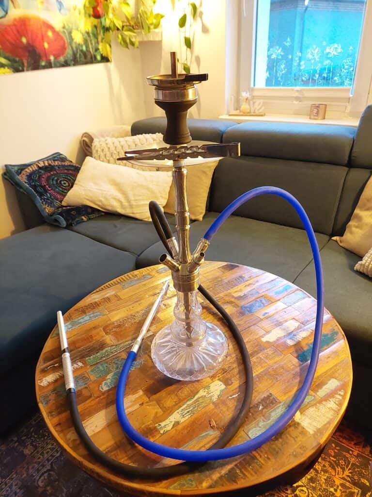 Shisha mit Glasbowl, Schlauch und Tabak auf Holztablett.