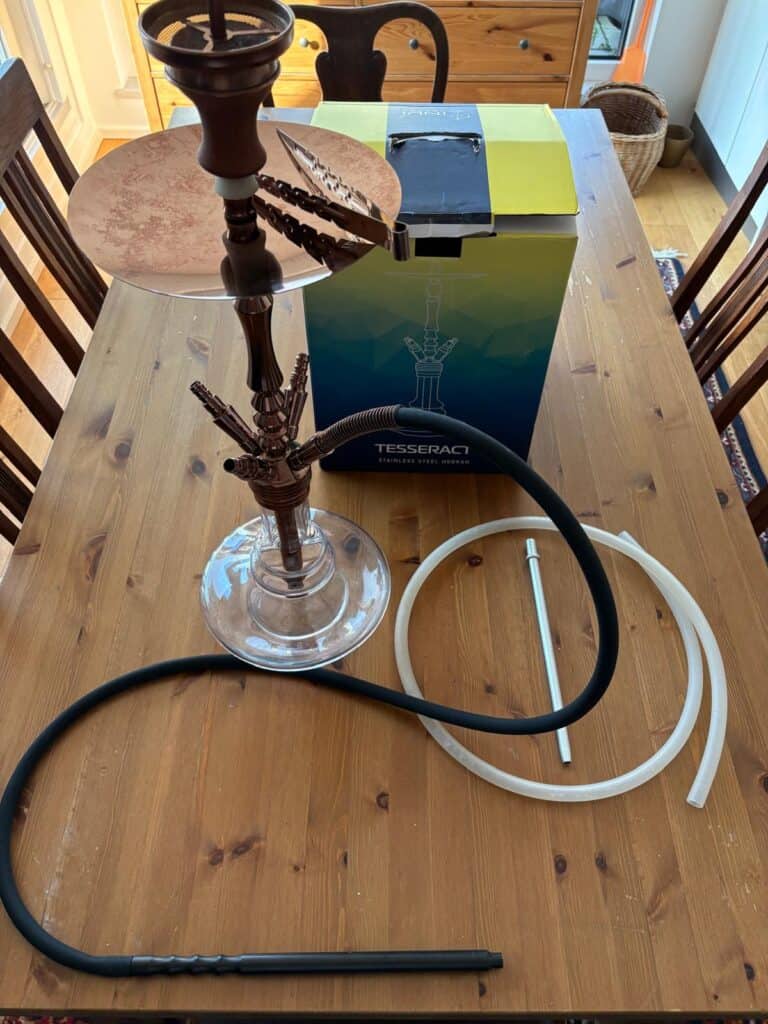 Shisha-Set mit Glasbowl, Schlauch und Zubehör auf Holztisch.