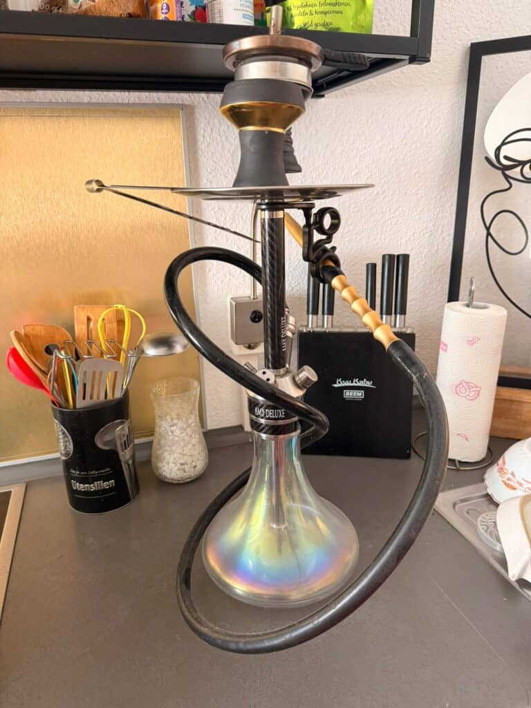 Shisha mit Glasbowl, Schlauch und Zubehör auf Tisch.