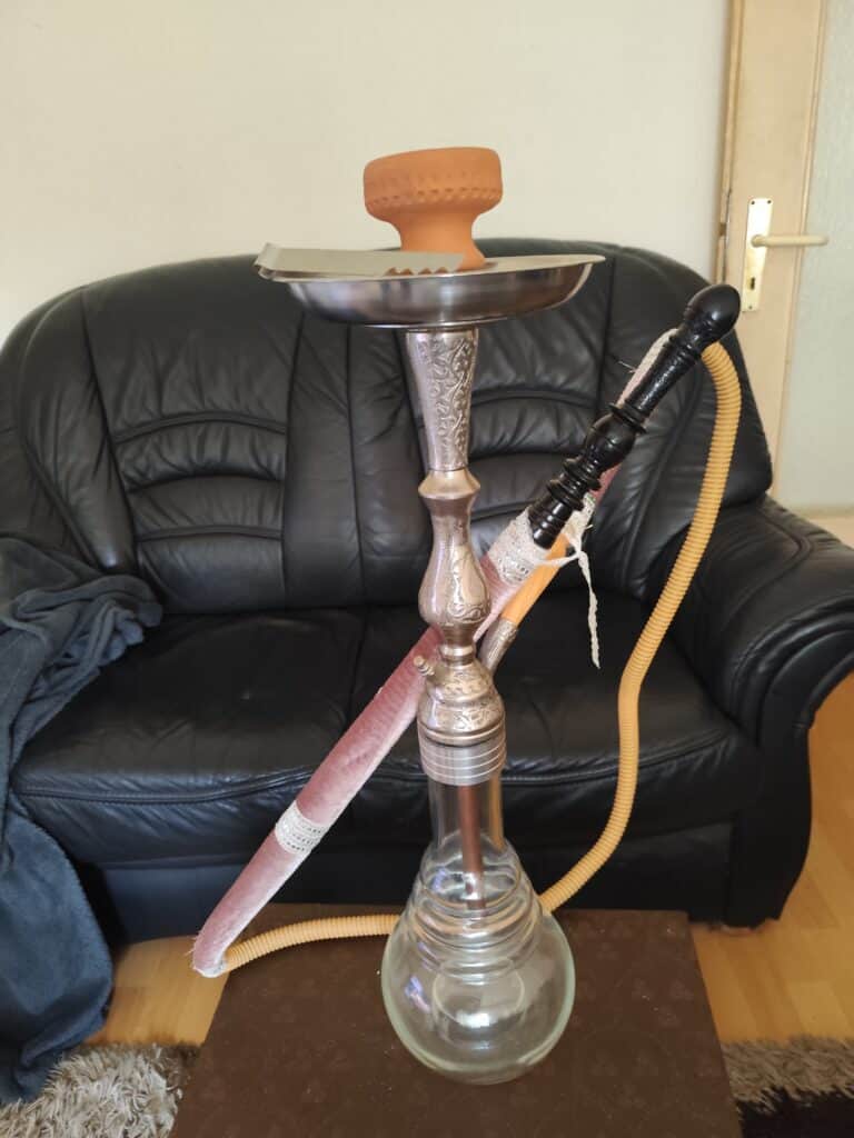 Shisha mit Glasbowl, Schlauch und Metallkopf auf Tisch.