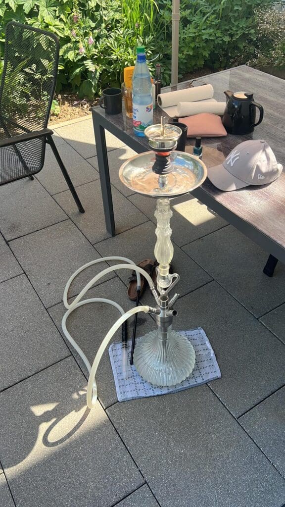 Wasserpfeife mit Glasbowl, Tabak, Zange und Zubehör im Außenbereich.