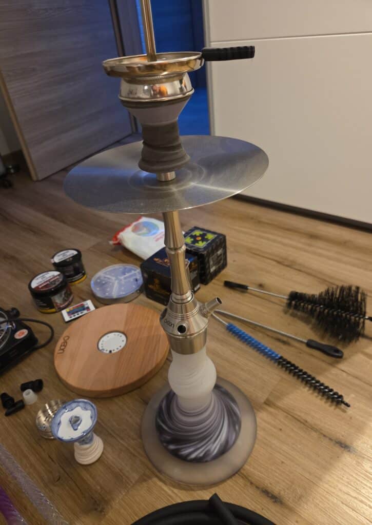 Shisha mit Glasbowl, Kamin, und Reinigungszubehör auf Boden.