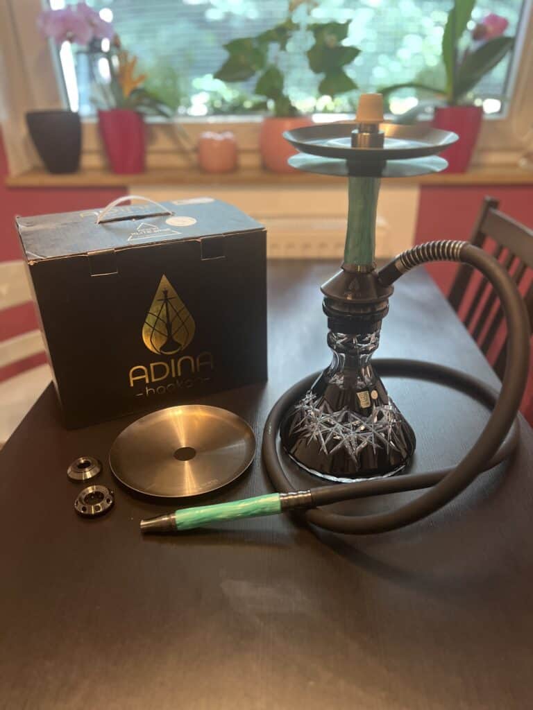 Shisha mit Glasbowl, Schlauch und Zubehör auf Tisch.