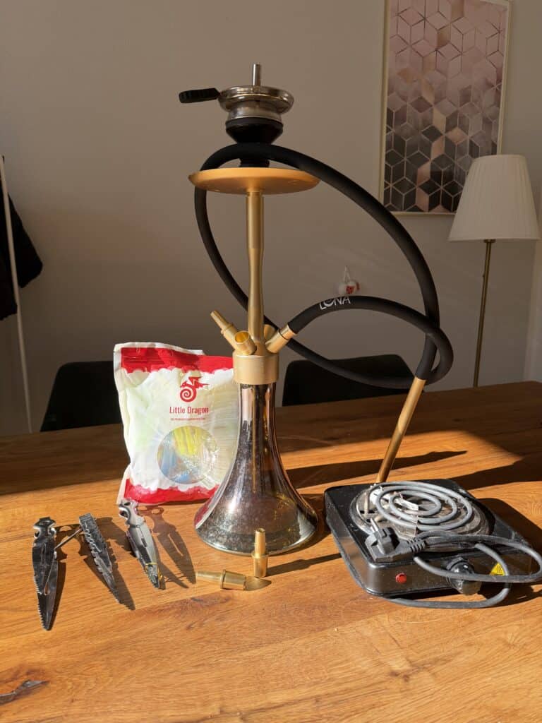 Shisha mit Glasbowl, Heizsystem und Zubehör auf Holztisch.