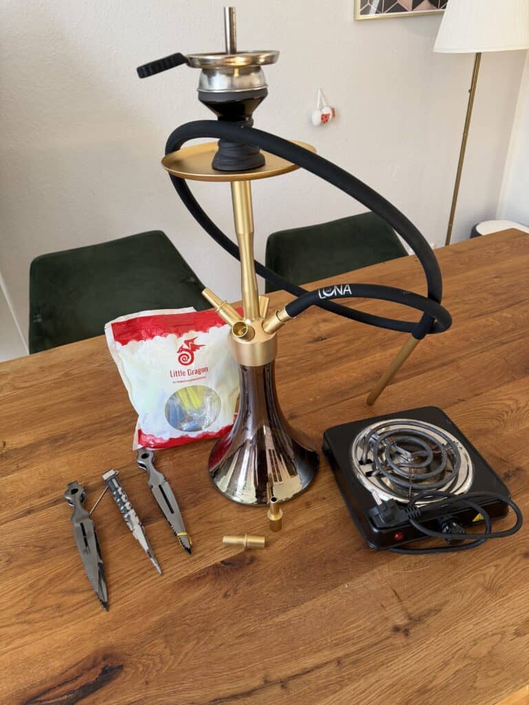 Shisha mit Glasbowl, Heizplatte und Werkzeugen auf Tisch.