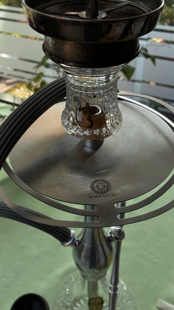 Detailaufnahme einer Shisha mit Glasbowl und Metallaufsatz auf einem Tisch.
