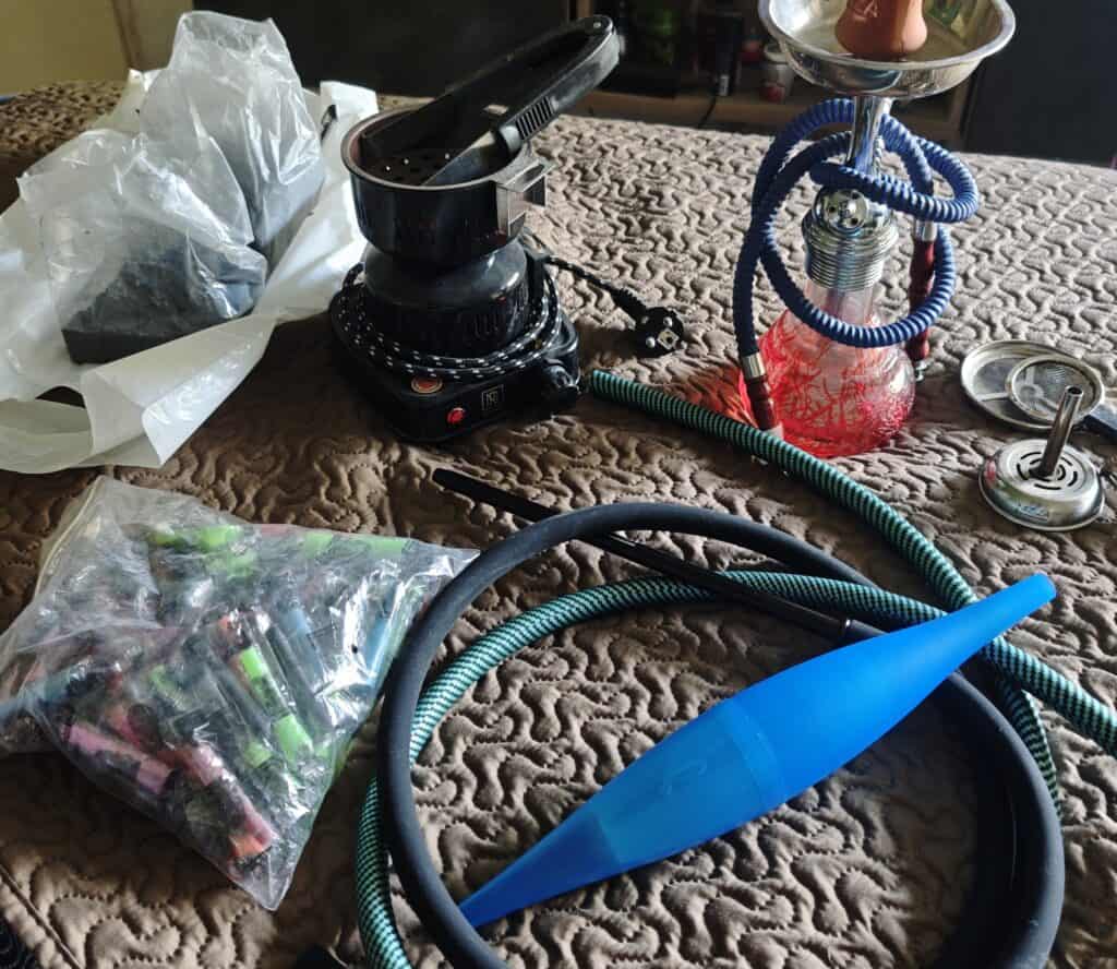 Verschiedene Shisha Teile, inklusive Glasbowl, Schlauch und Kohlezange.