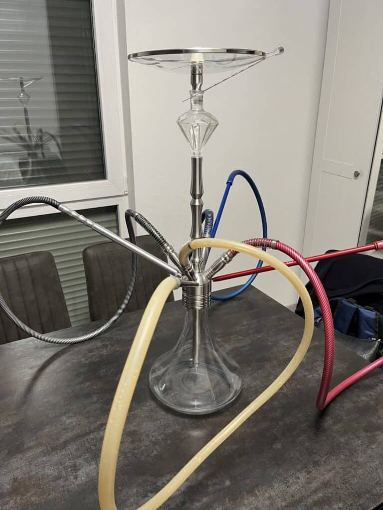 Shisha-Kopf mit Glasbowl, Schläuchen und Metallstange auf Tisch.