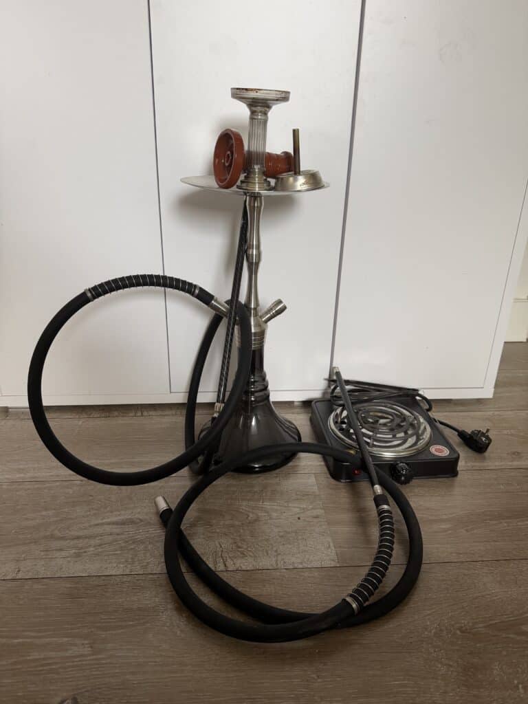 Shisha mit Heizplatte, Schlauch und Glasbowl, auf Holzboden.