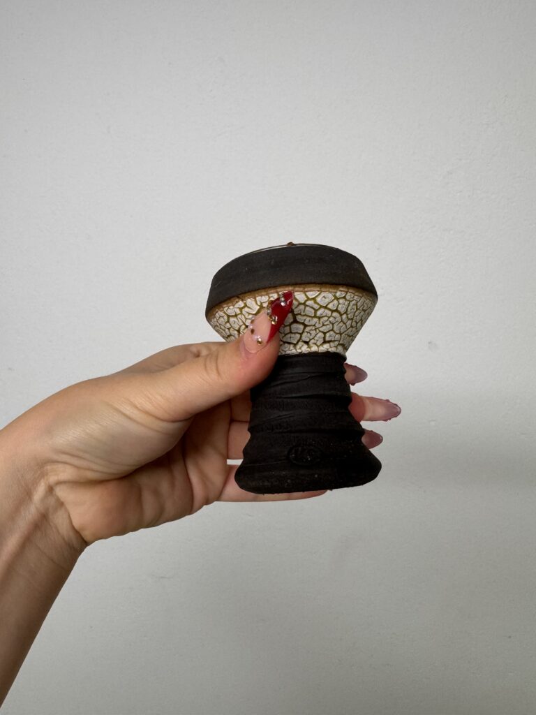 Hand hält eine schwarze und beige Glasbowl für Shisha mit Crackmuster.