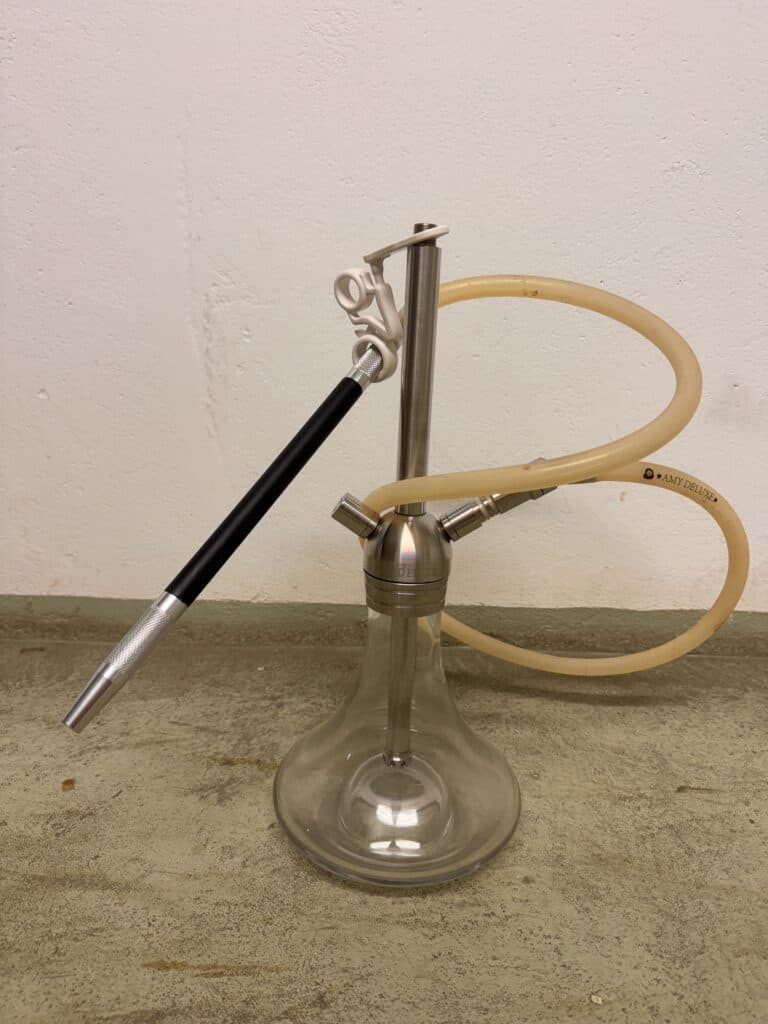 Shisha mit Glasbowl, Metallrohr und Silikonschlauch auf Boden.