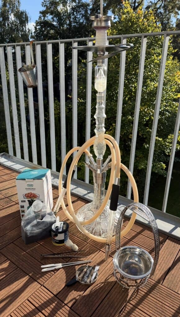 Shisha mit Glasbowl, Schlauch und Zubehör auf Balkon im Freien.