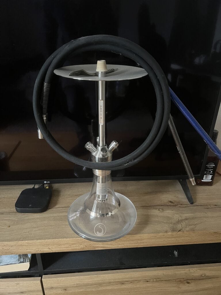 Shisha mit Glasbowl, Schlauch und Metallstück auf Holz.