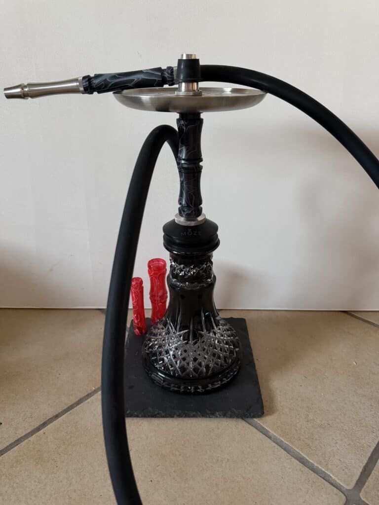 Shisha mit Glasbowl, Schlauch und Zubehör auf Boden.