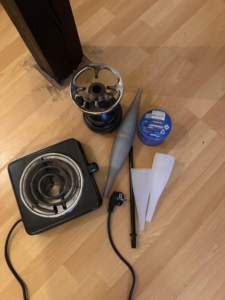 Verschiedene Shisha Zubehörteile auf Holzboden, inklusive Heizgerät und Glasbowl.