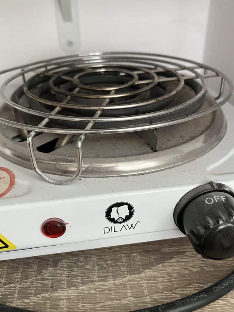 Kleines elektrisches Kochfeld mit Metallgitter und Drehknopf.