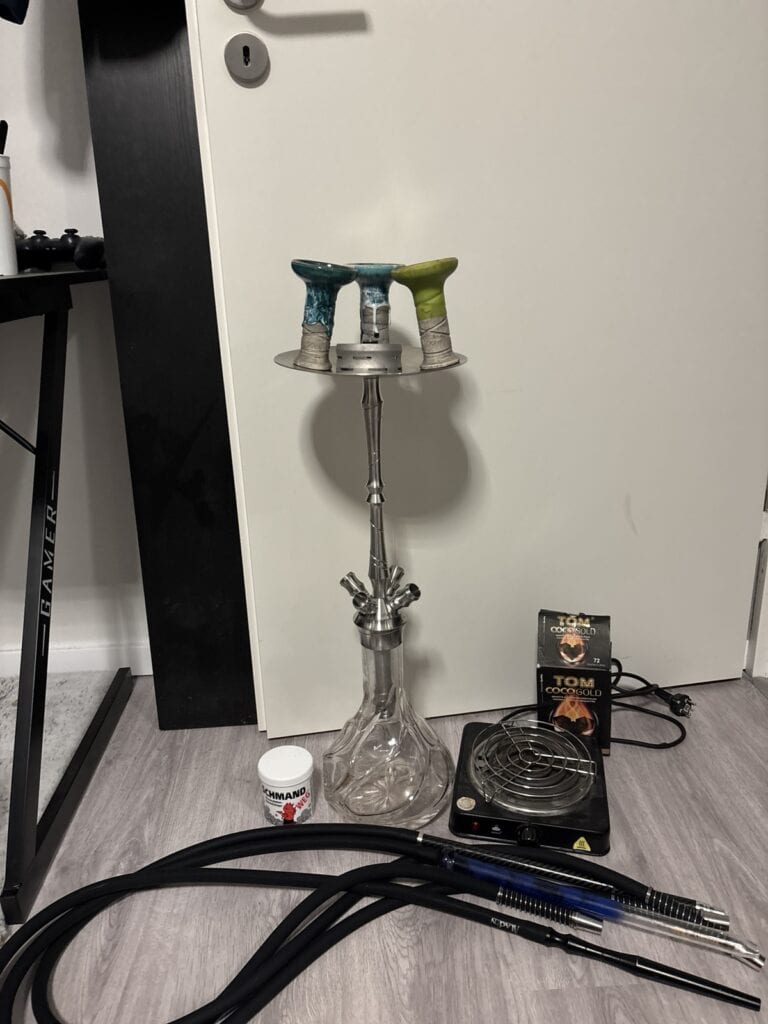 Shisha-Set mit Glasbowl, Schlauch und Heizplatte auf Boden.