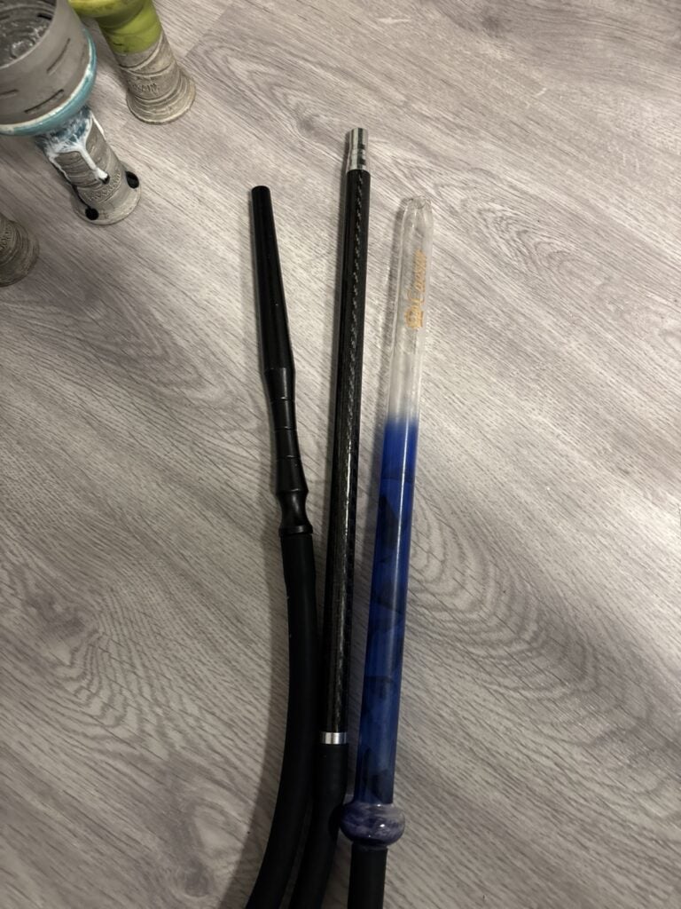 Verschiedene Shisha-Teile auf Holztisch, inklusive Glasbowl und Schlauch.