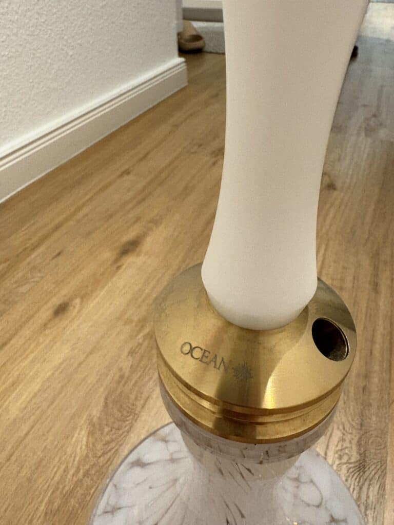 Shisha mit weißem Glasbowl und goldener Basis auf Holzboden.