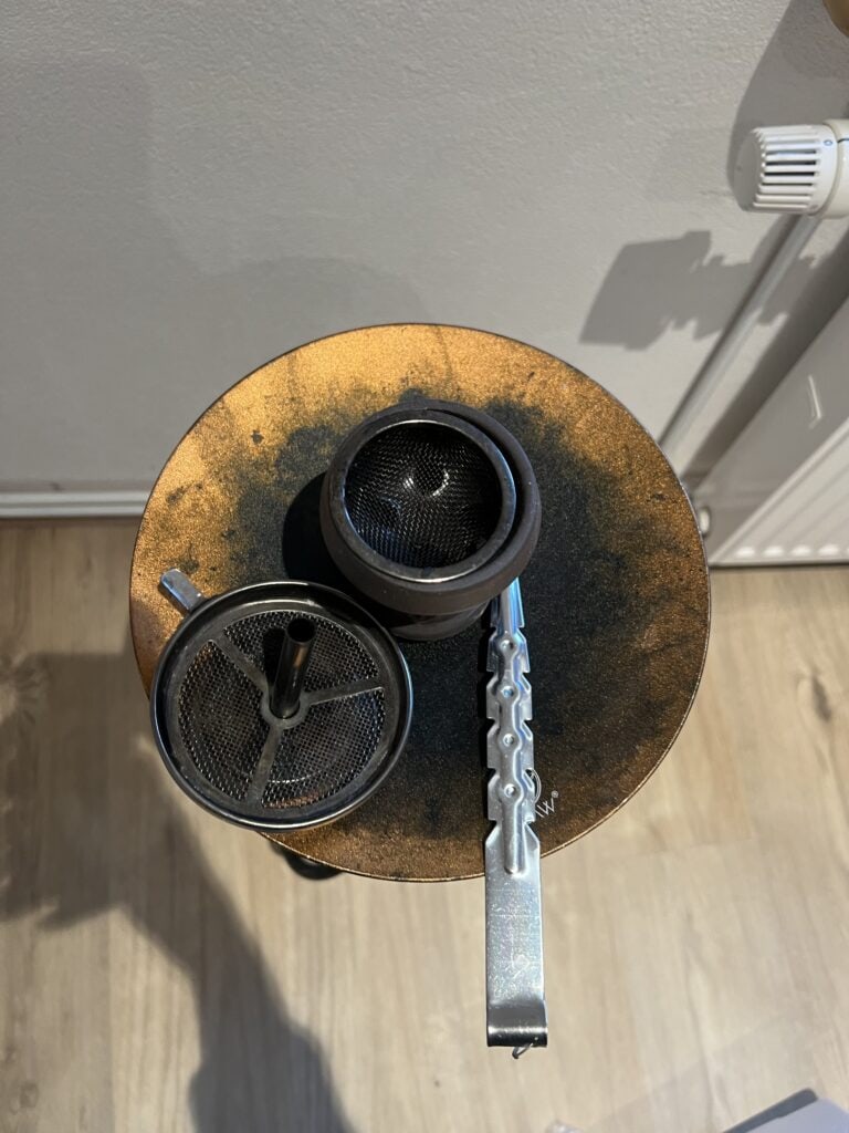 Rostige Shisha-Glasbowl mit Metallzubehör auf Holz.