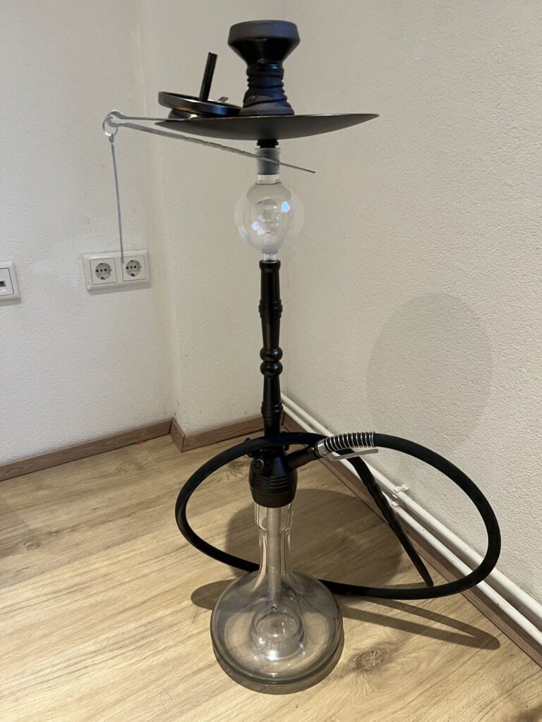 Shisha mit Glasbowl, Schlauch und Kopf, auf Holzboden.
