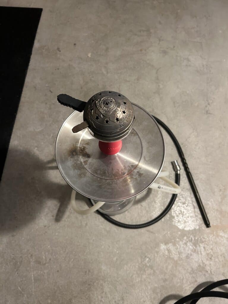Shisha-Set mit Glasbowl, Schlauch und Heizkopf auf Betonboden.