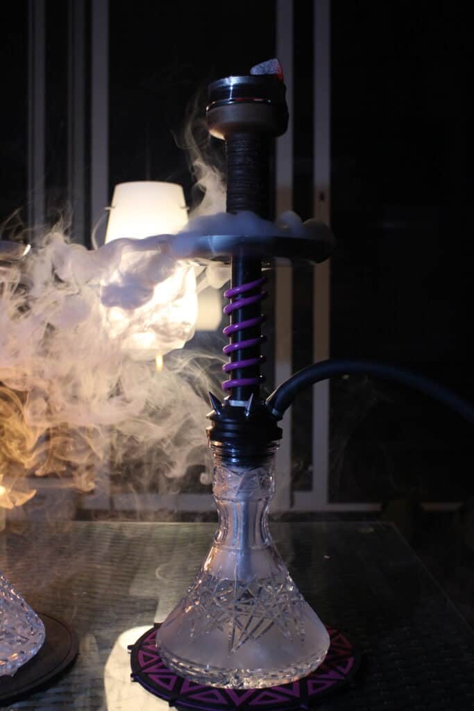 Schwarze Shisha mit Glasbowl und Rauchentwicklung im dunklen Raum.