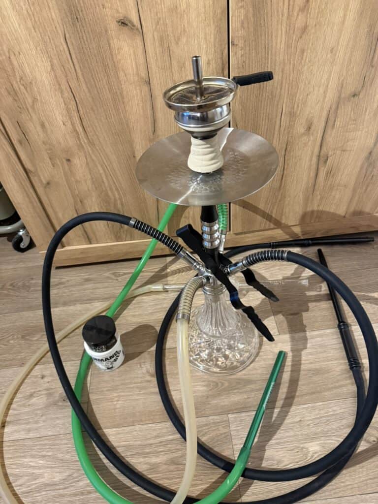 Shisha mit Glasbowl, Schlauch und Zubehör auf Holzboden.