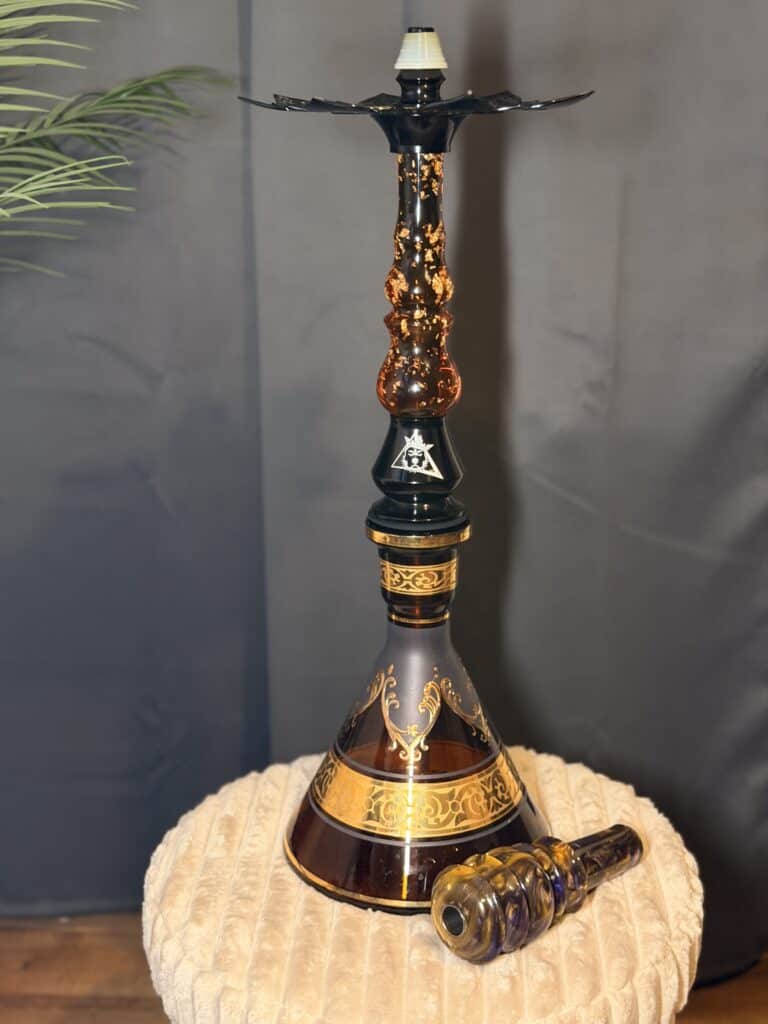Schöne Shisha mit goldenen Akzenten und Glasbowl auf einem beige Kissen.