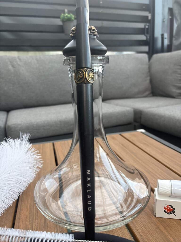 Moderne Shisha mit schwarzem Metallrohr und Glasbowl auf Holztisch.