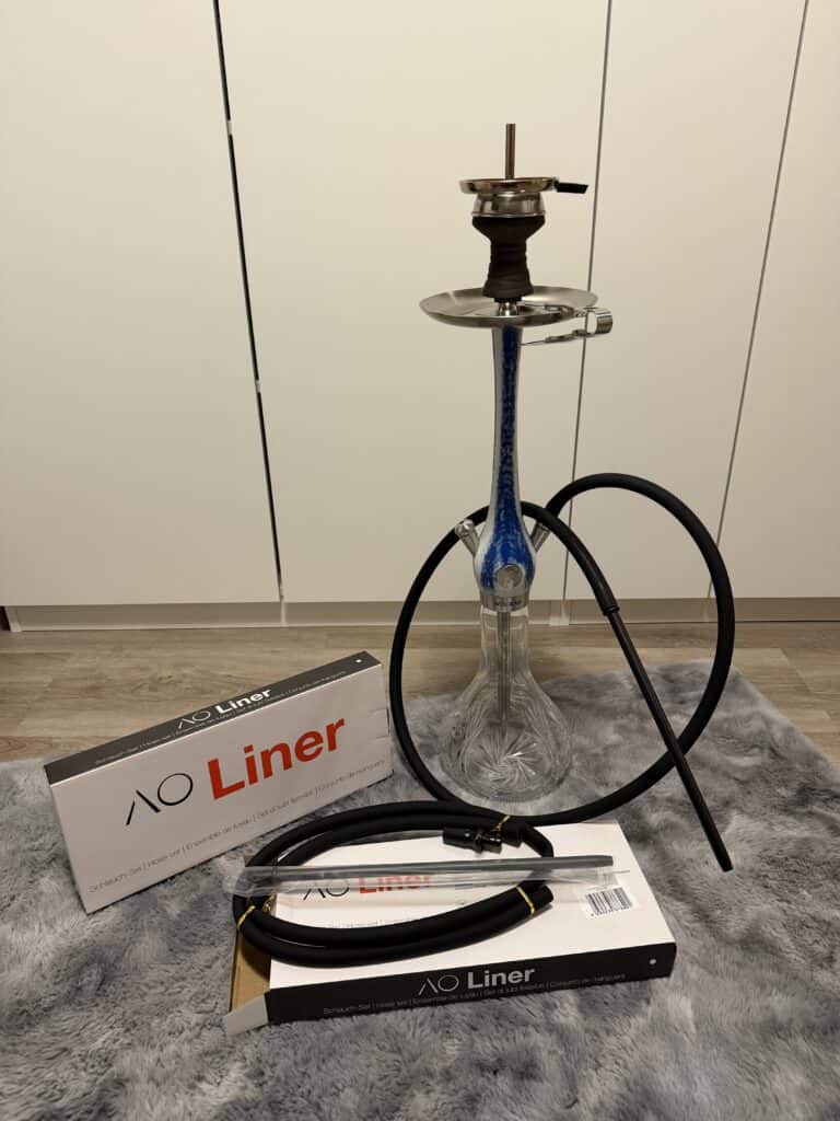 Shisha-Kopf mit Glasbowl, Schlauch und Zubehör, auf Teppich.
