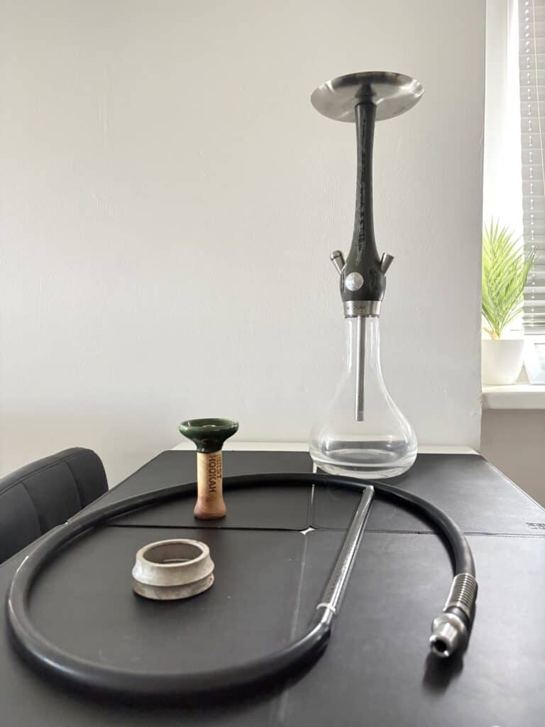 Shisha mit Glasbowl, Schlauch und Kopf auf Tisch.