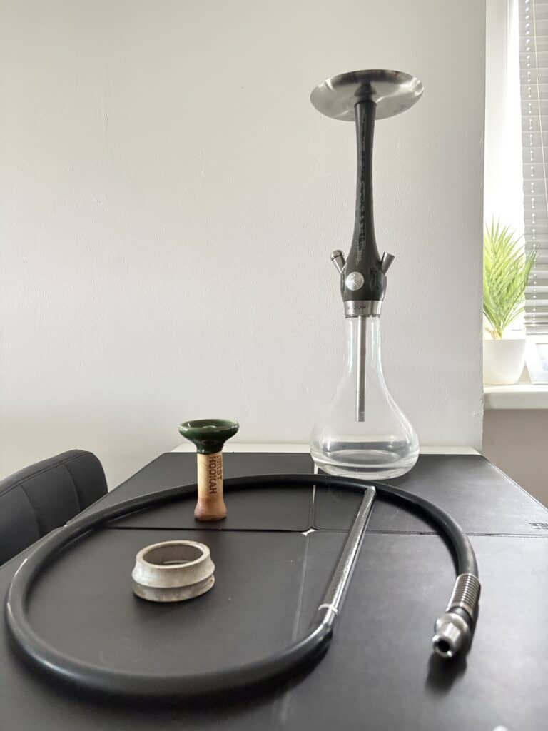Shisha mit Glasbowl, Schlauch und Kopf auf Tisch.