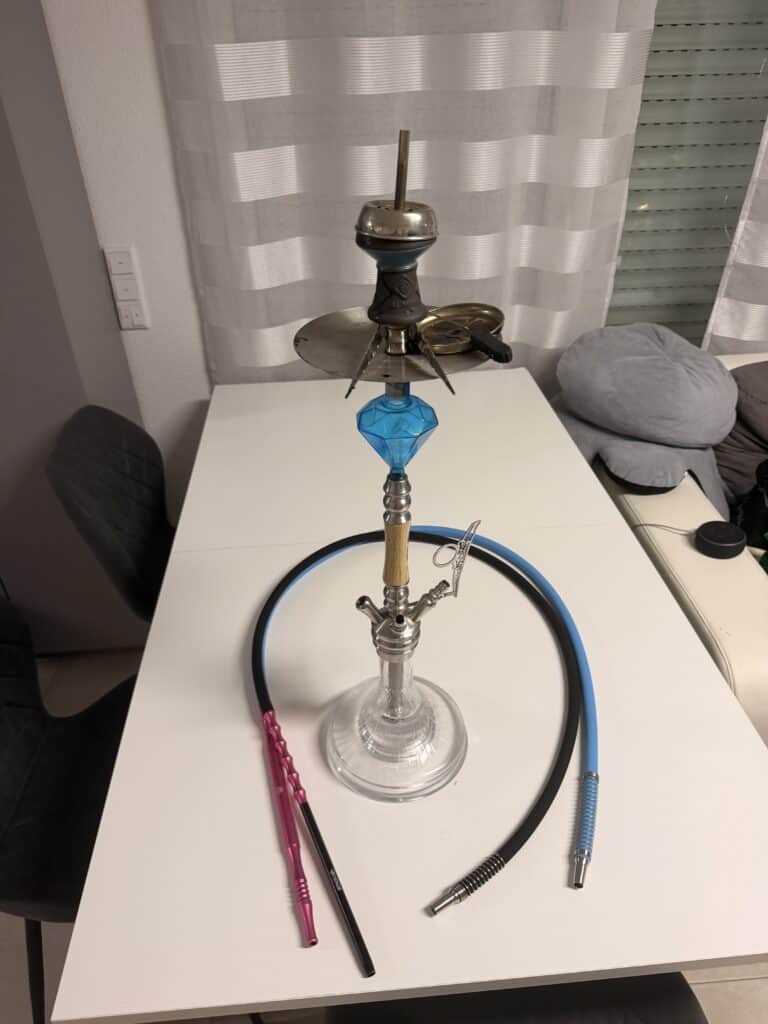 Shisha mit Glasbowl, Schlauch und Zubehörelemente auf Tisch.