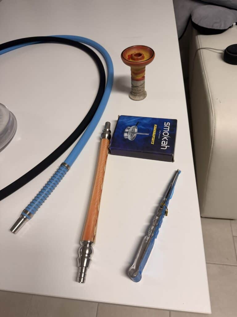 Verschiedene Shisha-Teile auf einem Tisch, inklusive Glasbowl und Schlauch.
