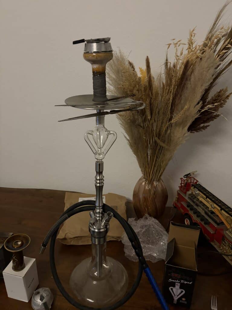 Shisha mit Glasbowl, Schlauch und Zubehör auf Tisch.