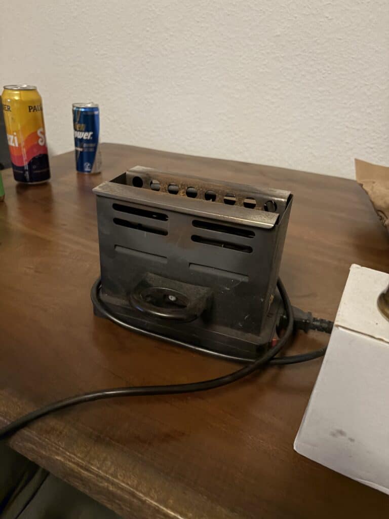 Elektrischer Grill auf Holztisch mit Kabel und Getränkedosen.