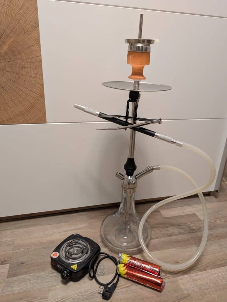 Shisha mit Glasbowl, Schlauch und Heizgerät auf Boden.
