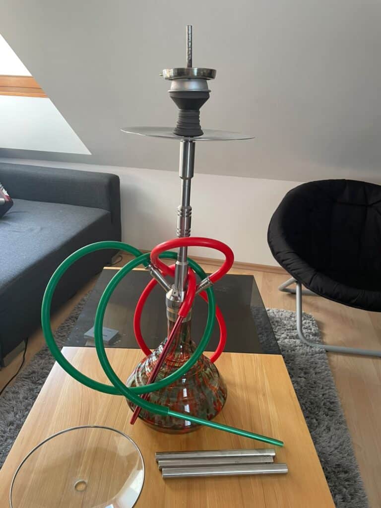 Shisha mit Glasbowl, Schlauch und Zubehör auf Tisch.