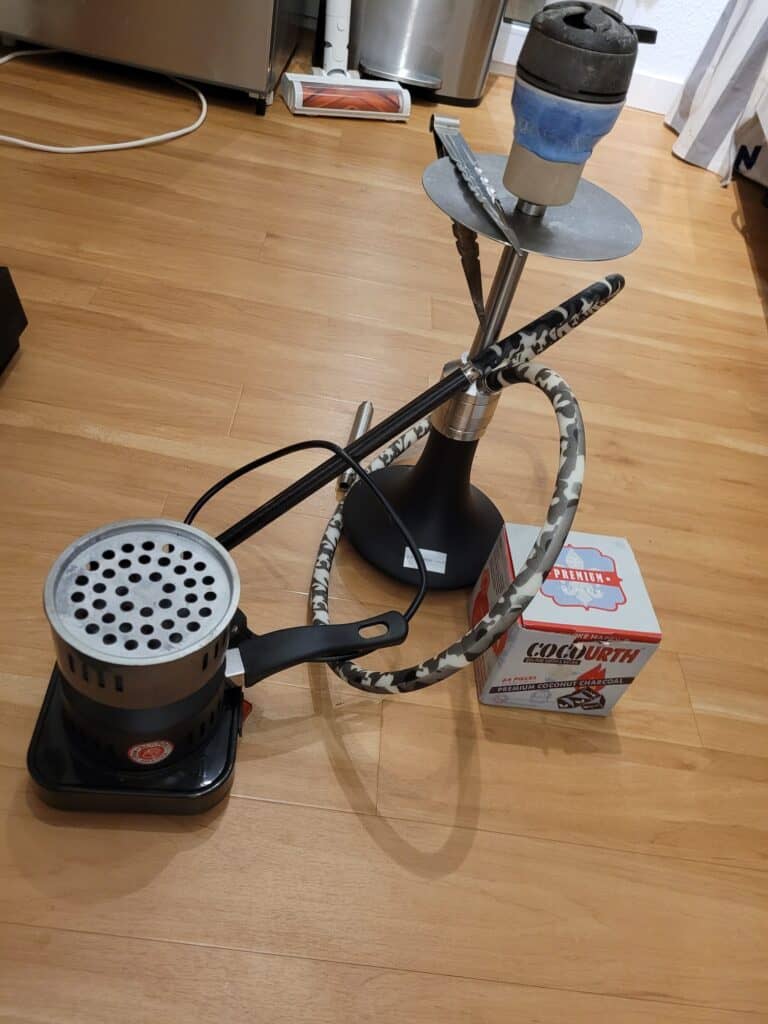 Shisha bowl with metal stem, hose, and coal tray auf Holzboden.