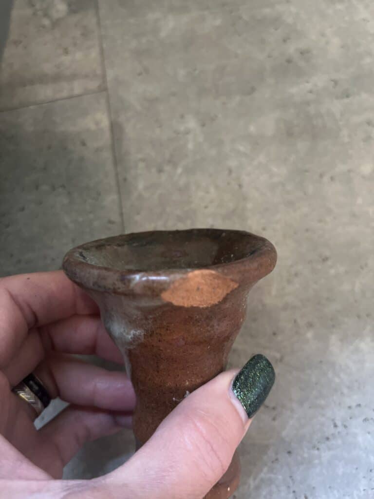 Hand hält eine alte, braune Shisha-Glasbowl vor einer Steinwand.