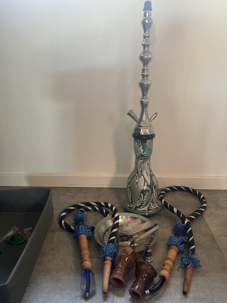 Shisha mit Glasbowl, Schlauch und Zubehör auf Boden.