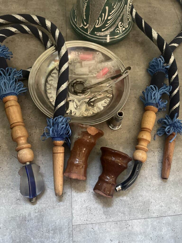 Verschiedene Shisha-Teile, inklusive Glasbowl, Schlauch und Holzadapter.