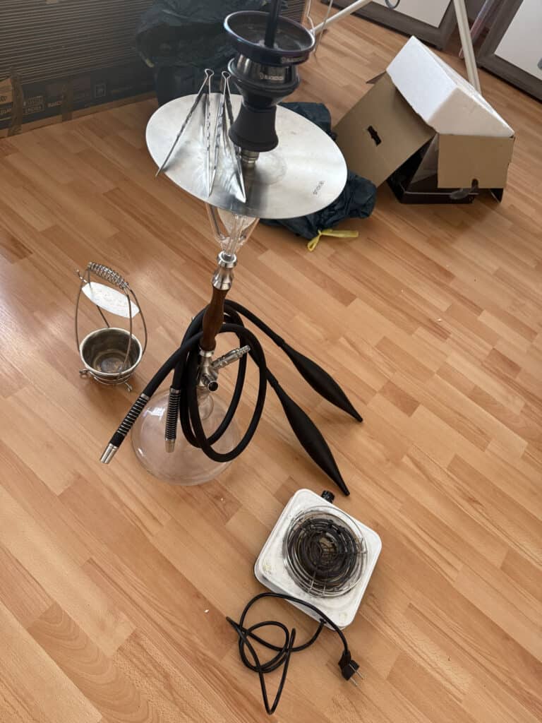 Shisha mit Glasbowl, Schlauch und Zubehör auf Holzboden.